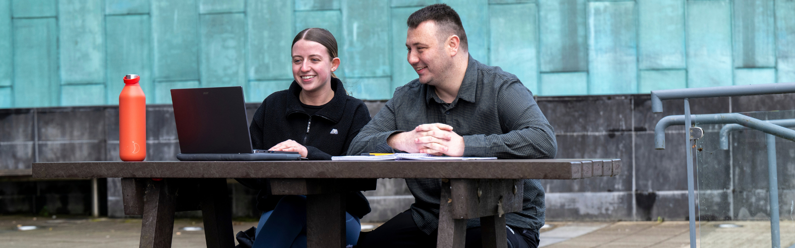 Image of 2 students sitting on an outdoor bench on campus