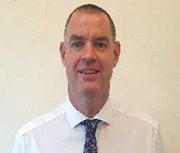 Professional headshot of a person wearing a white shirt and tie against a plain background