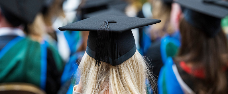 Back of students head with blonde hair wearing graduation cap and gown 