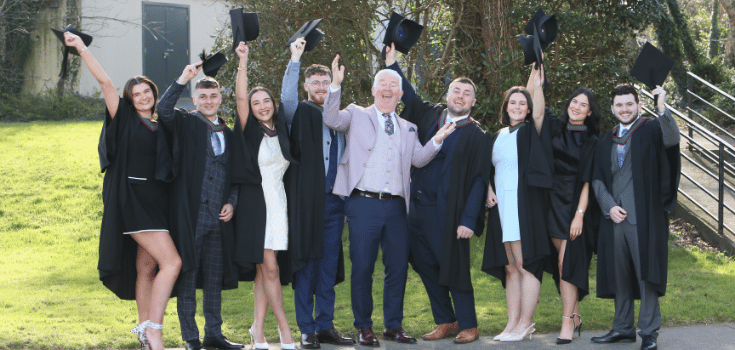 students in graduating gowns throwing hats in air an smiling