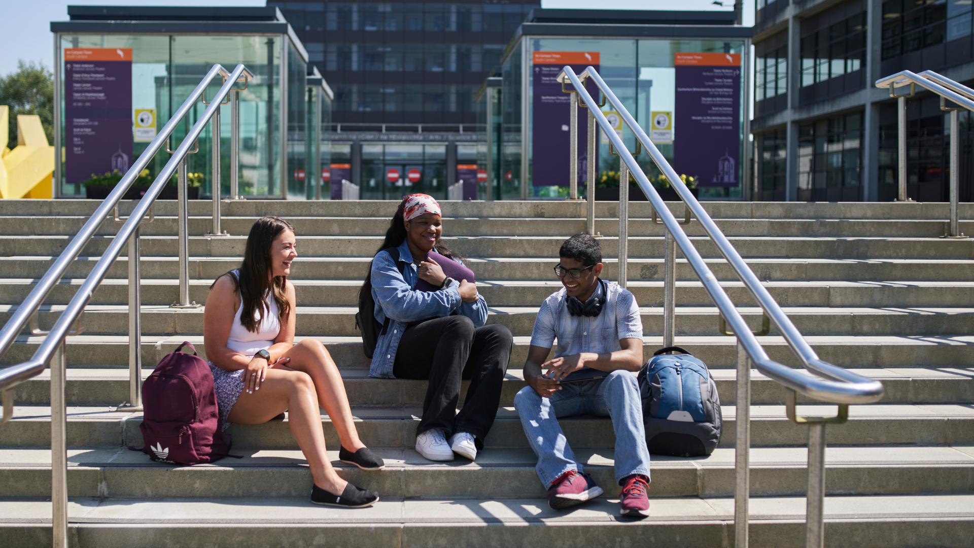 three students sitting on the steps in front of the big yellow thing