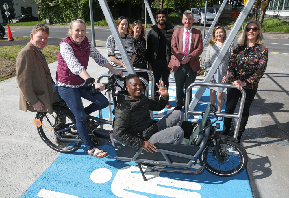 An image of nine people standing and sitting around an accessible bike shelter on the University of Galway campus