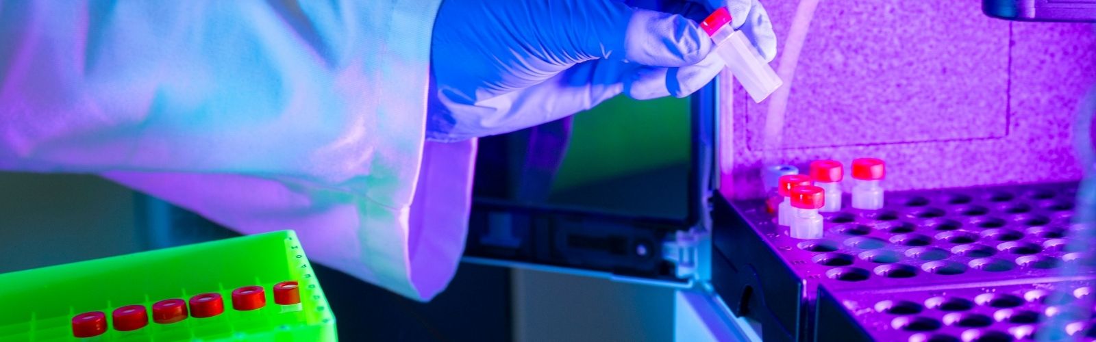 An image of a gloved hand transferring a vial with a red cap into a mass spectrometer