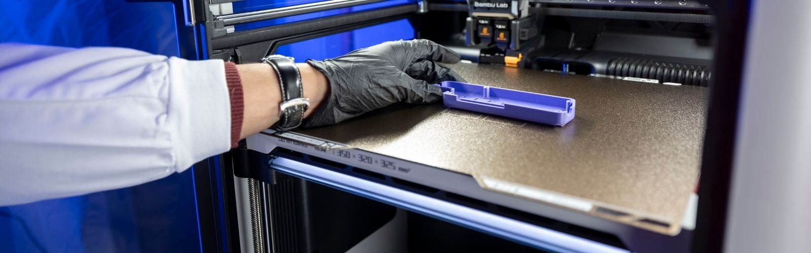 An image of a hand taking a purple 3D printed object from a 3D printer