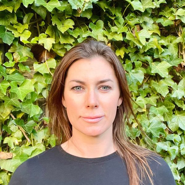 A headshot of Dr. Angela Mc Ardle, in colour, with green hedges in the background